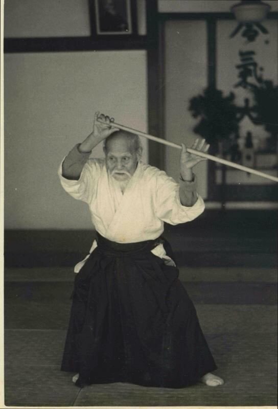 Morihei Ueshiba (O-Sensei) ejecutando una postura de bastón (Jō) en el dojo